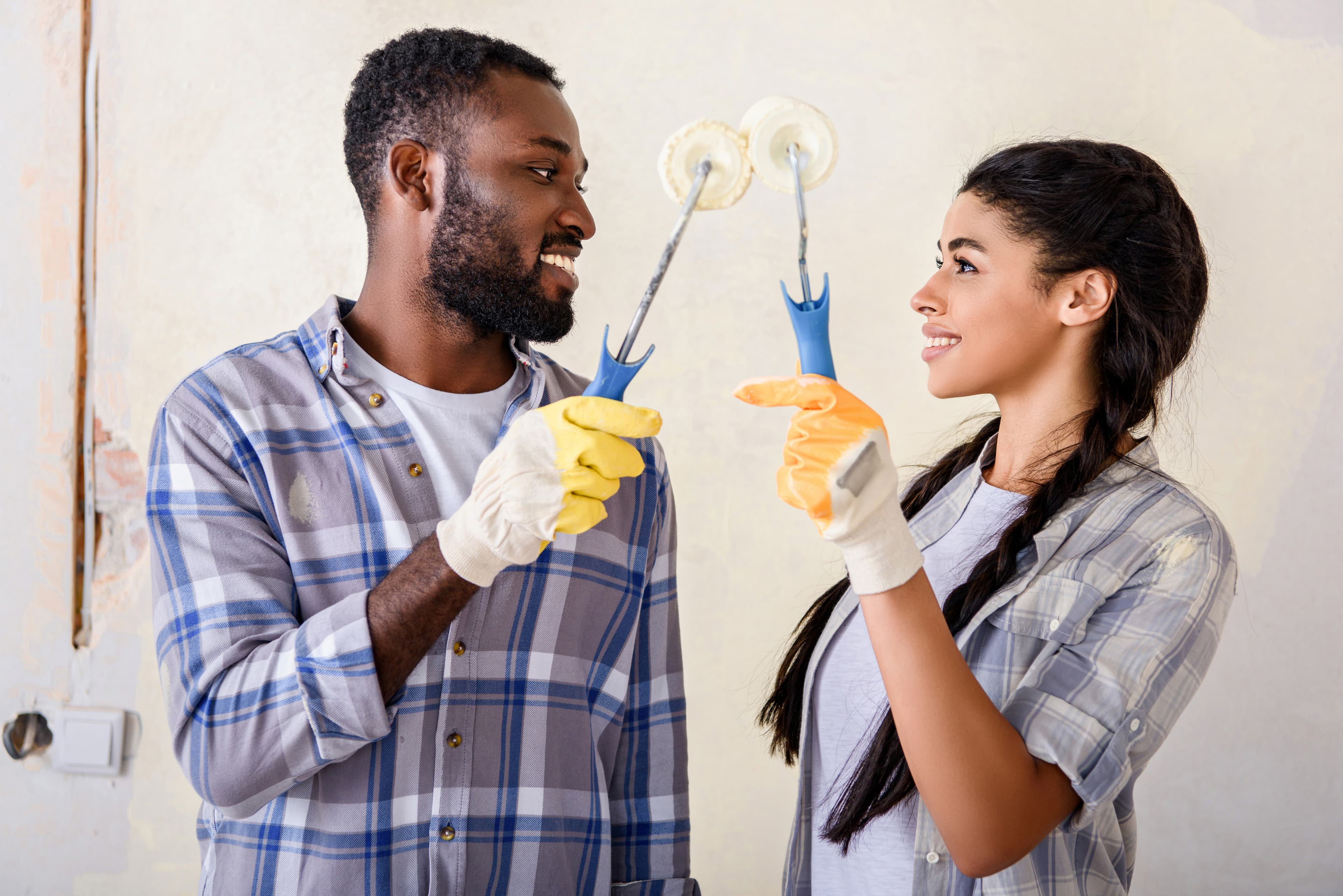 Smiling couple holding paint rollers while renovating